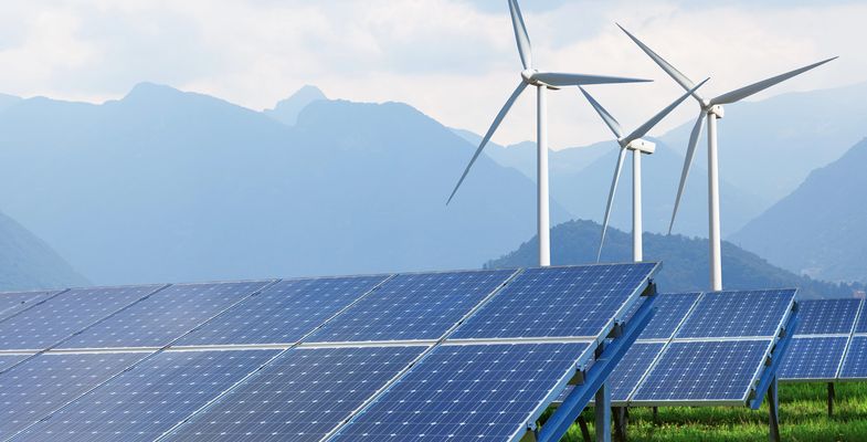 Solar panels and wind turbines with mountains in background